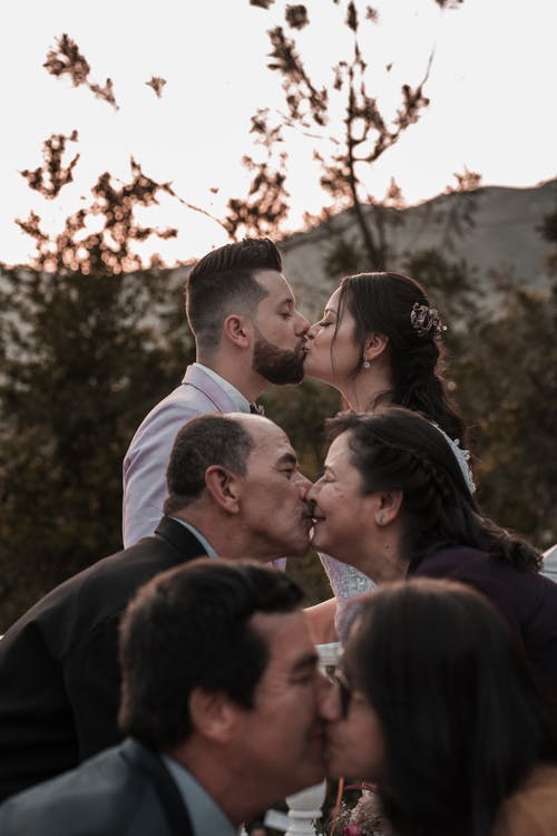 优雅的种族新婚夫妇和父母在婚礼当天在户外接吻 · 免费素材图片