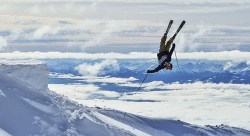 不可识别的滑雪者在白雪皑皑的山峦中执行倒置技巧 · 免费素材图片