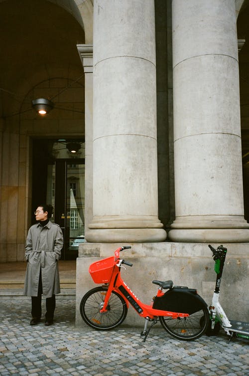 站立在停放的自行车附近和大厦与专栏的无法认出的妇女 · 免费素材图片