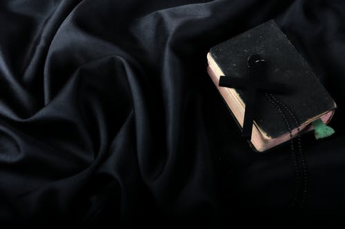 硬封面圣经上的黑色十字在黑色纺织之上 · 免费素材图片