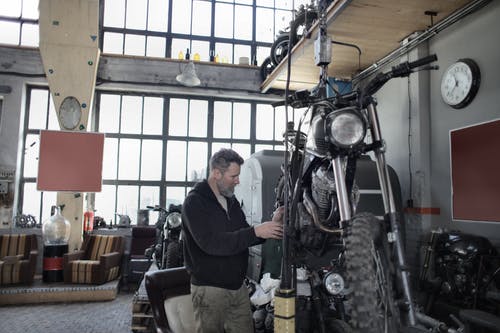 大胡子的机修工检查摩托车在车库里 · 免费素材图片
