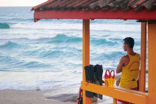 白色背心的女人坐在海滩上的棕色木椅上 · 免费素材图片