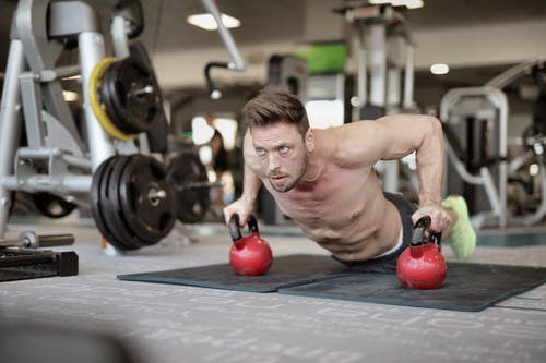 做在壶铃的严肃的肌肉运动员俯卧撑在现代健身房 · 免费素材图片