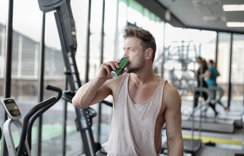 疲倦的年轻男运动员在健身房锻炼后休息时喝能量饮料 · 免费素材图片