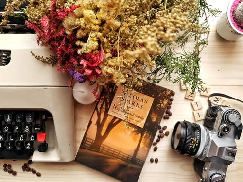 束鲜花和书安排与老式打字机和相机木制的桌子上 · 免费素材图片