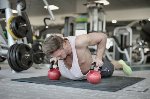做在壶铃的俯卧撑的肌肉运动员在健身房 · 免费素材图片