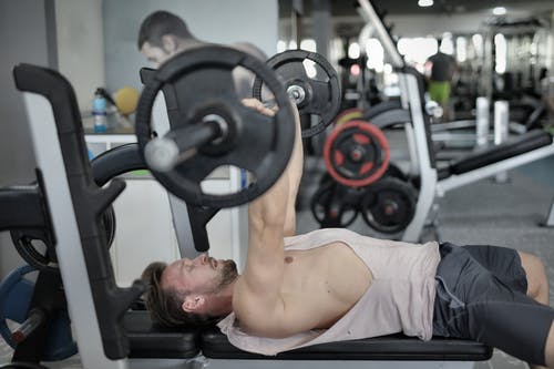 在现代健身房锻炼期间做卧推的强壮的运动员 · 免费素材图片