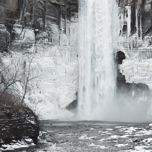 黑夹克的人站在瀑布附近的积雪的地面上 · 免费素材图片