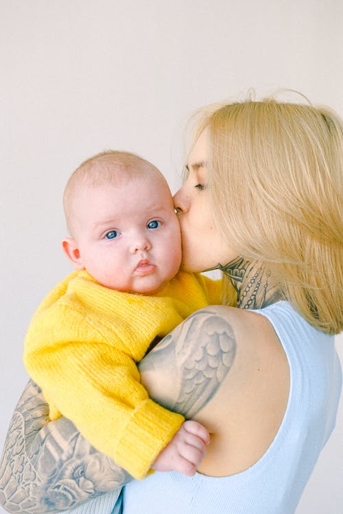 爱纹身的妈妈在房间里怀里亲吻婴儿婴儿 · 免费素材图片