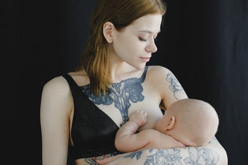 纹身的年轻母亲，穿着胸罩和母乳喂养新生儿在工作室 · 免费素材图片