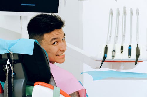 坐在牙科椅的快乐的种族人在现代牙医办公室 · 免费素材图片