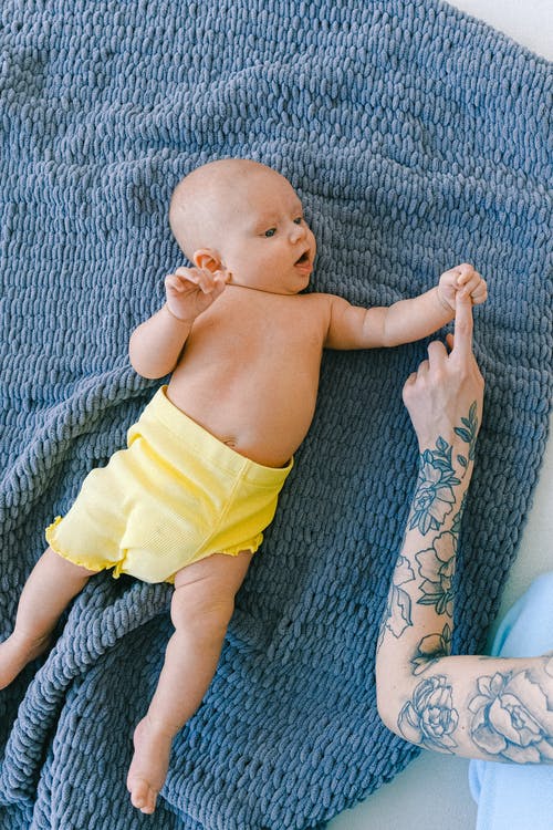 裁剪纹身女性与好奇的婴儿宝宝躺在床上的柔软毯子上 · 免费素材图片
