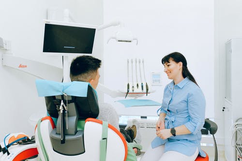性格开朗的口腔科医生和坐在牙科椅上的病人交谈 · 免费素材图片