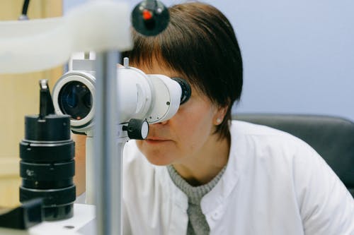 不可识别的女科学家通过裂隙灯显微镜观看 · 免费素材图片