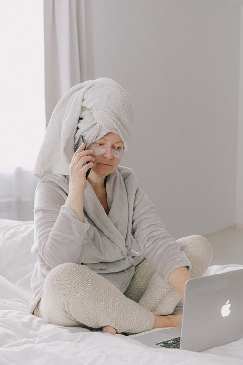 有膝上型计算机和智能手机的年迈的女性在床上 · 免费素材图片