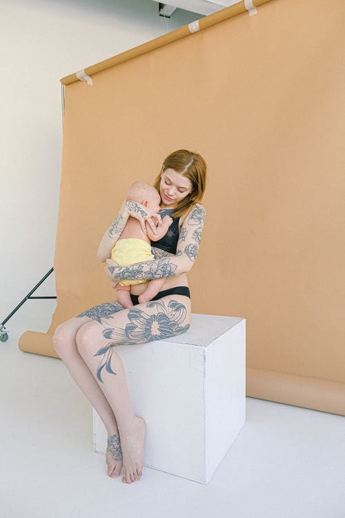 年轻的纹身的母亲在内衣拥抱新生婴儿在现代工作室 · 免费素材图片