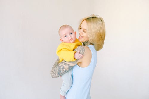 性格开朗的纹身的女性在灰色背景下怀抱中拥抱的小宝贝 · 免费素材图片