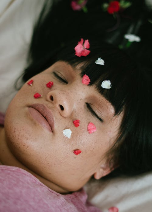 感性丰满的民族女士躺在床上，花瓣在脸上，闭着眼睛放松 · 免费素材图片