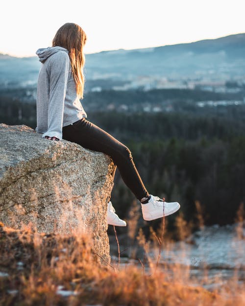 灰色连帽衫和黑色的裤子，坐在岩石上的女人 · 免费素材图片