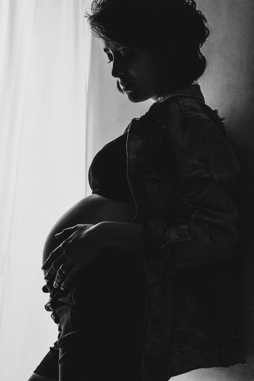 站立在屋子里的愉快的年轻怀孕的女性爱抚的腹部 · 免费素材图片