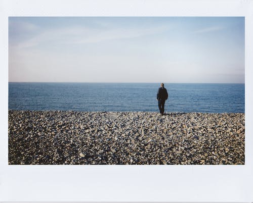 穿黑夹克的男人站在灰色的岩石海岸 · 免费素材图片