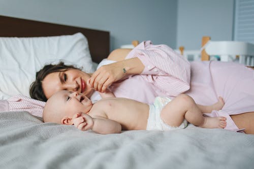 母亲躺在她婴儿旁边的床上 · 免费素材图片