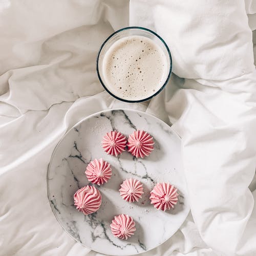 早餐在弄皱的床单上的拿铁咖啡的美味蛋白甜饼 · 免费素材图片