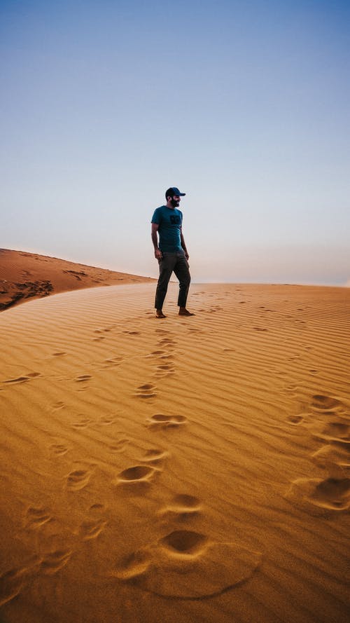 匿名男子享受沙漠景色站在沙丘上 · 免费素材图片