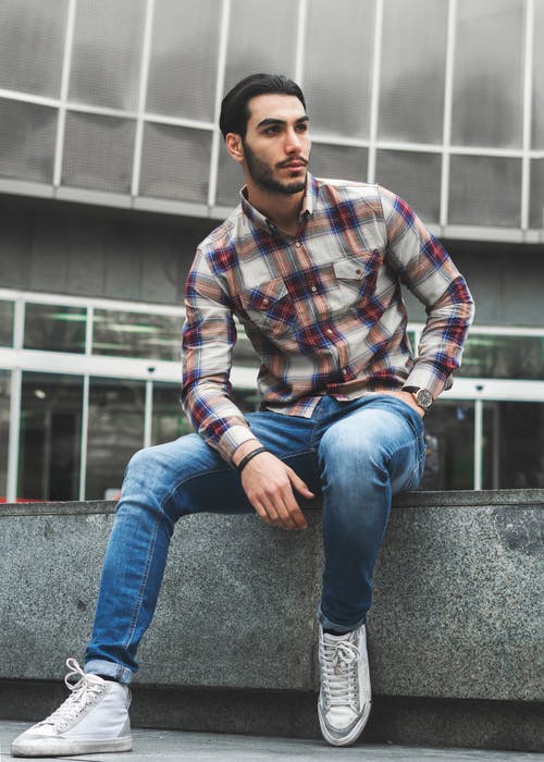 格子衬衫和蓝色牛仔牛仔裤，坐在混凝土上的男人 · 免费素材图片