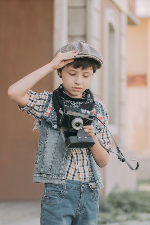 拿着黑色和灰色照相机的蓝色牛仔夹克的男孩 · 免费素材图片