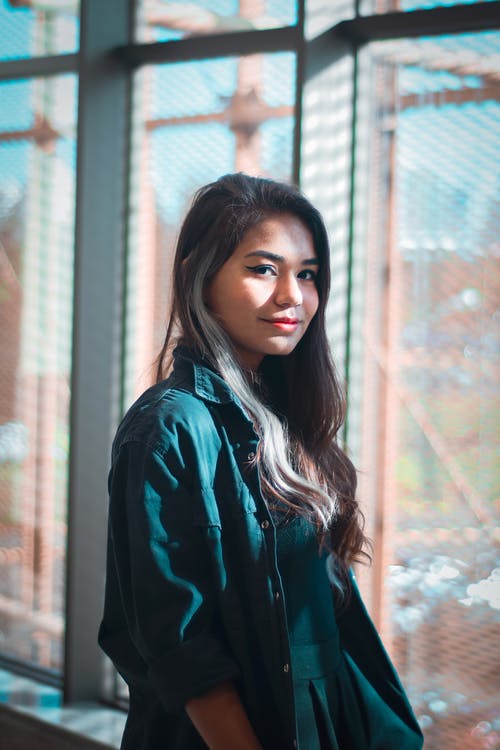 站立在窗口附近的快乐的年轻种族夫人在晴天 · 免费素材图片