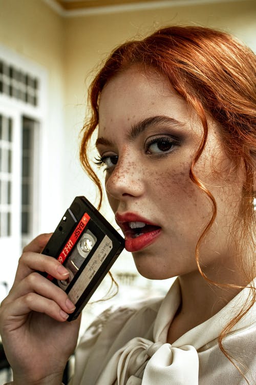 女人拿着黑色和红色的盒式磁带 · 免费素材图片