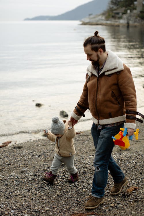 父亲带着玩具在水附近的海滩上散步时带着玩具 · 免费素材图片