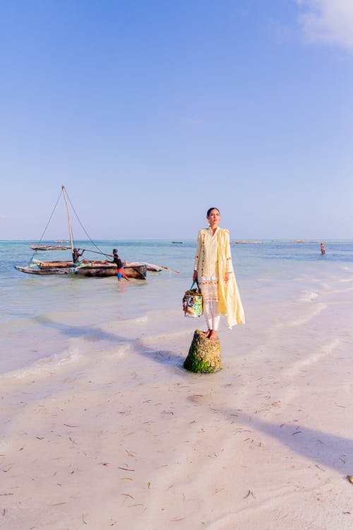 女人站在一块岩石在沙滩上 · 免费素材图片