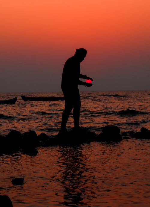 男子站在海滩上在日落时的剪影 · 免费素材图片