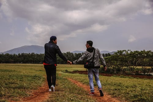 男子手牵着手在绿色草地上行走 · 免费素材图片