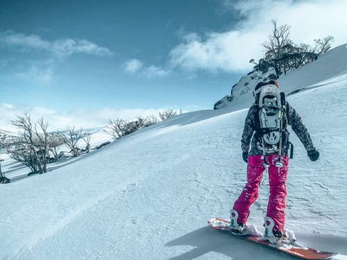 黑夹克和粉红色的裤子，站在积雪的地面滑雪板上的人 · 免费素材图片
