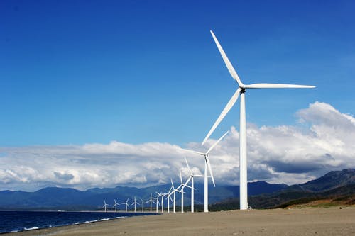 白色风力发电机在水体附近的灰色沙滩上 · 免费素材图片