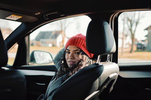 灰色风衣和红色针织帽坐在汽车座椅上的女人 · 免费素材图片