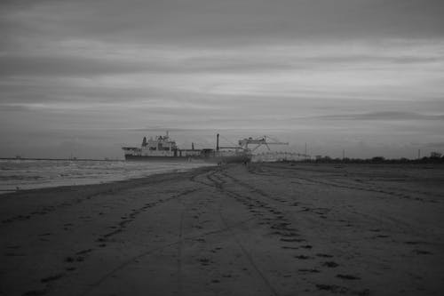 海滩与海上船的灰度照片 · 免费素材图片
