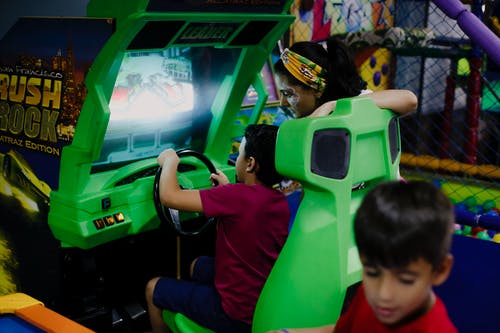 匿名男孩在母亲和兄弟姐妹附近玩赛车模拟器 · 免费素材图片