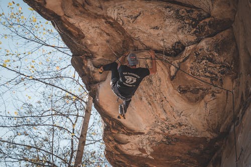 在锻炼期间在岩石下攀爬的动机年轻登山者 · 免费素材图片