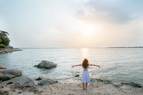 白衬衫站在水体附近的灰色岩石上的女人 · 免费素材图片