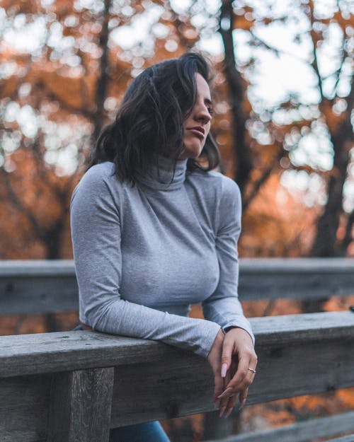 女人我灰色长袖衬衫，倚在木栅栏上 · 免费素材图片