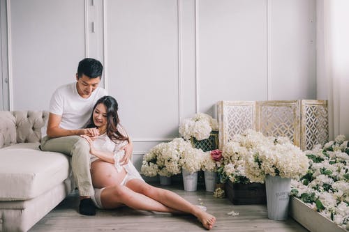 坐在花的客厅里的微笑怀孕夫妇 · 免费素材图片