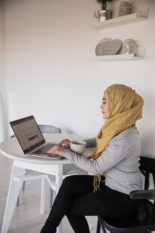 在家里喝咖啡休息时间在笔记本电脑上打字的穆斯林女商人 · 免费素材图片