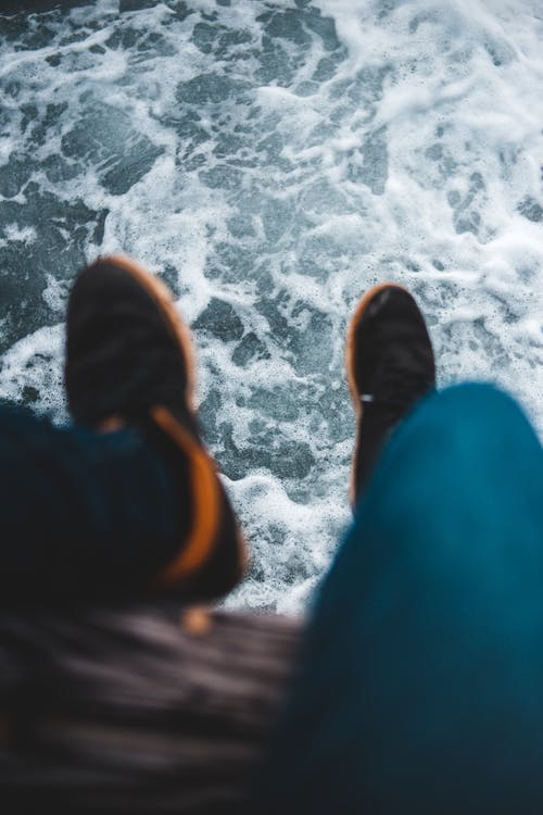 蓝色的裤子和棕色的鞋子，坐在悬崖上的人 · 免费素材图片