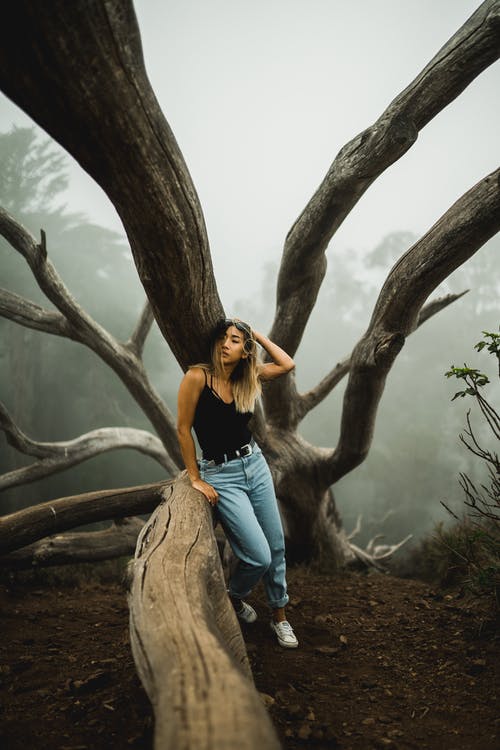 黑色背心和蓝色牛仔牛仔裤，倚在树上的女人 · 免费素材图片