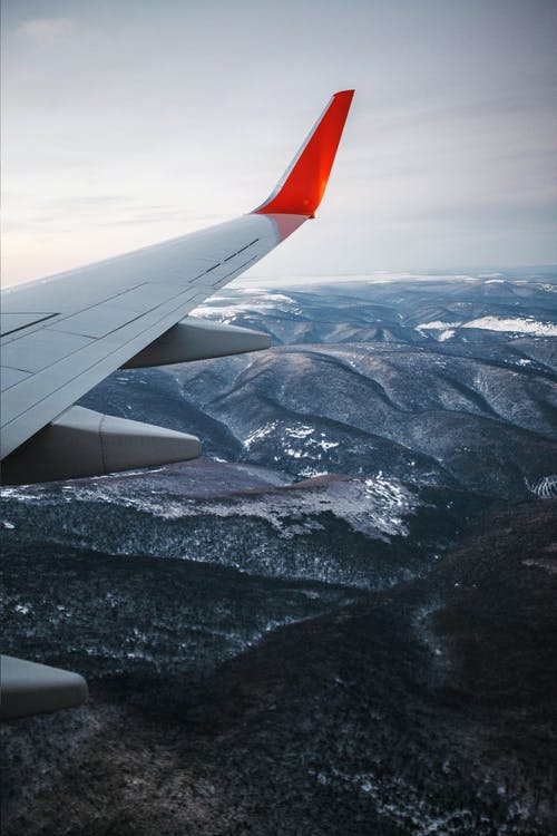 白色和红色飞机的机翼，越过积雪覆盖的山脉 · 免费素材图片