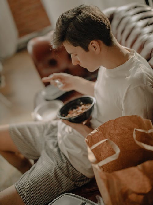 坐在棕色沙发椅子上的白船员脖子t恤的男孩 · 免费素材图片